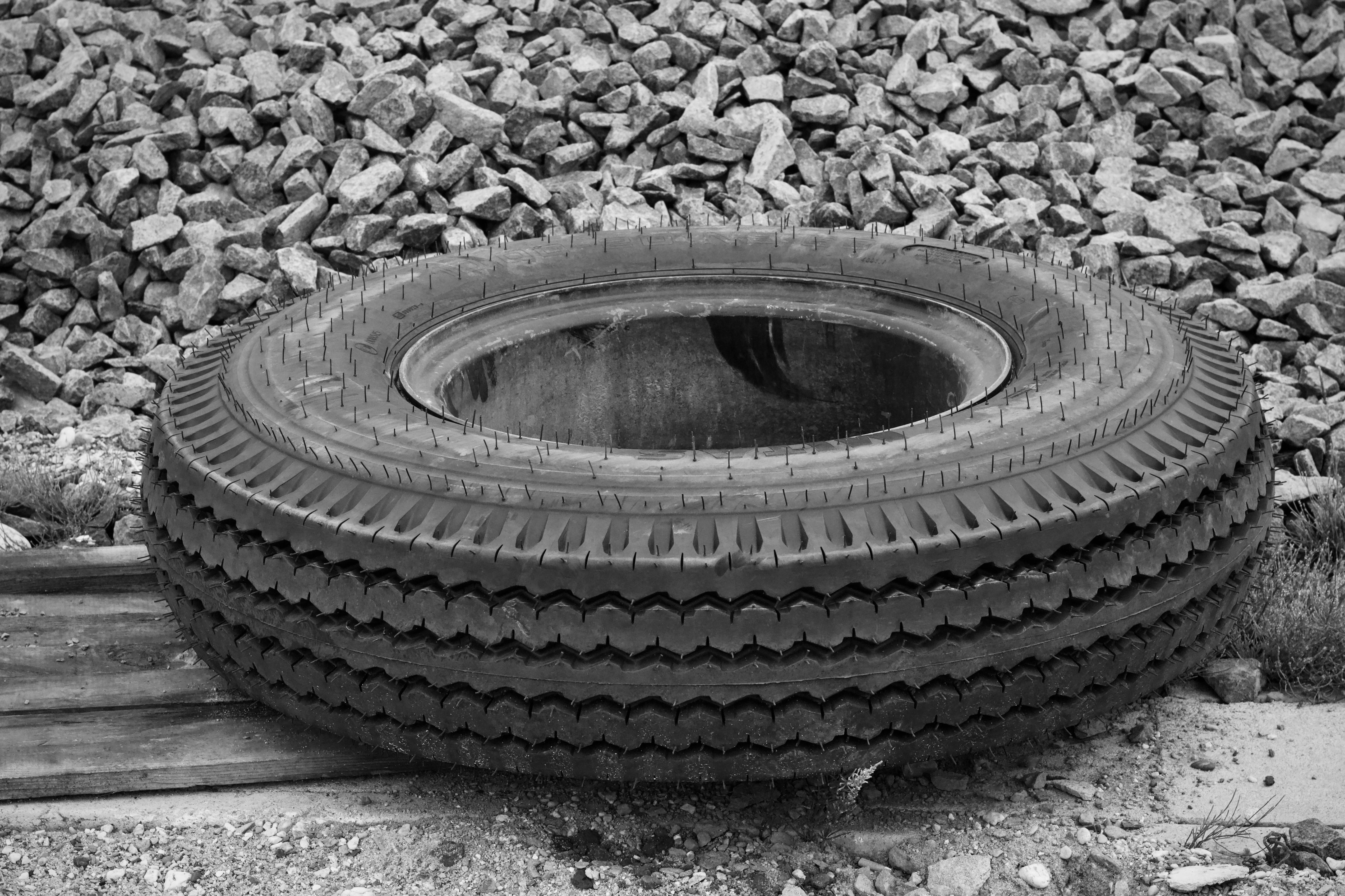 Black and white photo of a large industrial tire resting on gravel, showcasing rugged texture and urban setting.