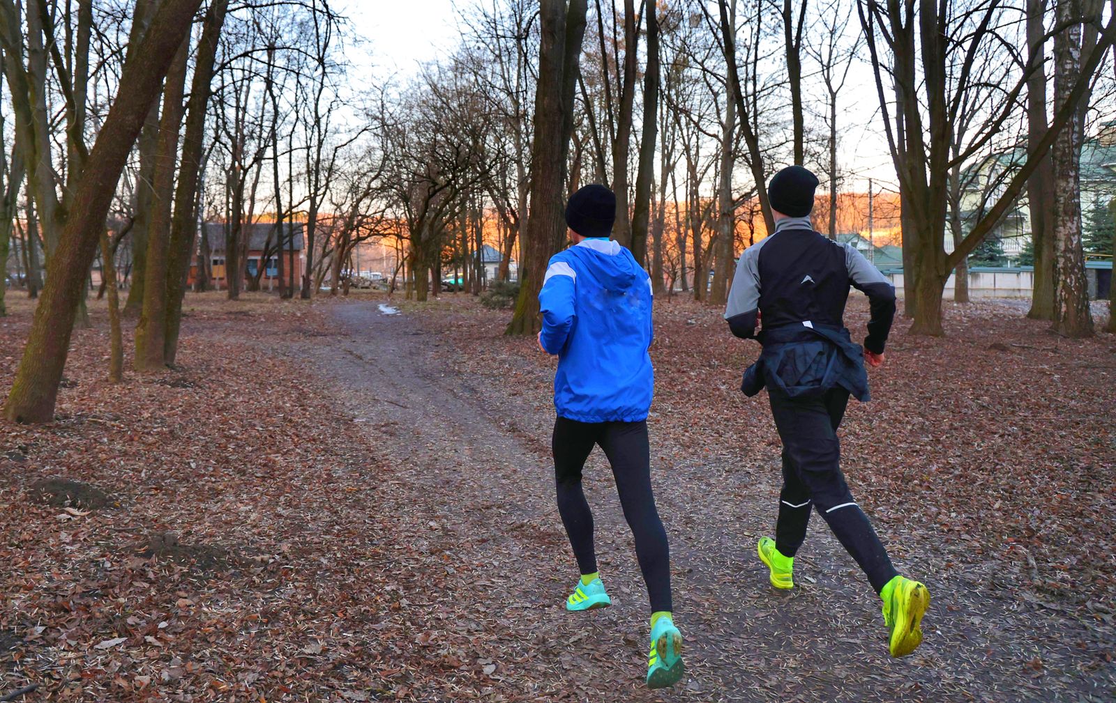 Two adults running on a leaf-covered park trail in autumn
