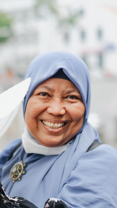 A cheerful woman wearing a blue hijab with a bright smile