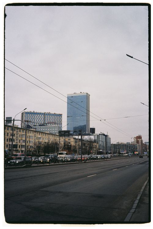Free City street view featuring a tall modern skyscraper amidst vehicles and buildings. Stock Photo