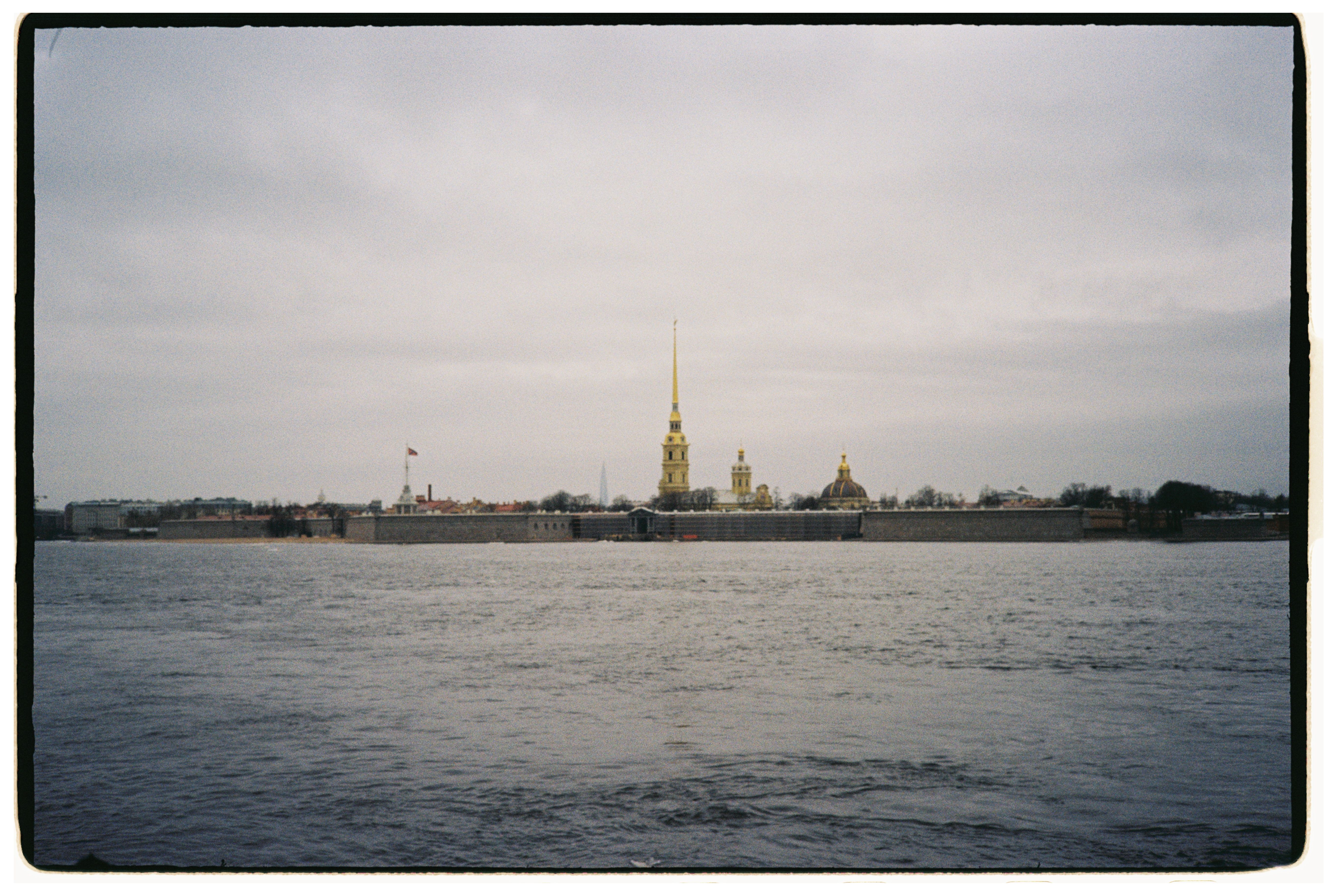 View of the Peter and Paul Fortress in Saint Petersburg across the river under a cloudy sky.