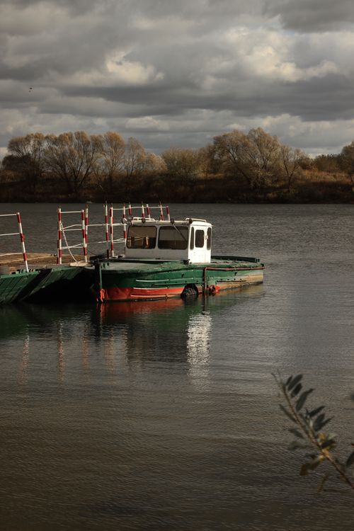 Free A small, vintage boat tied to a pier on a calm lake under a dramatic cloudy sky. Stock Photo