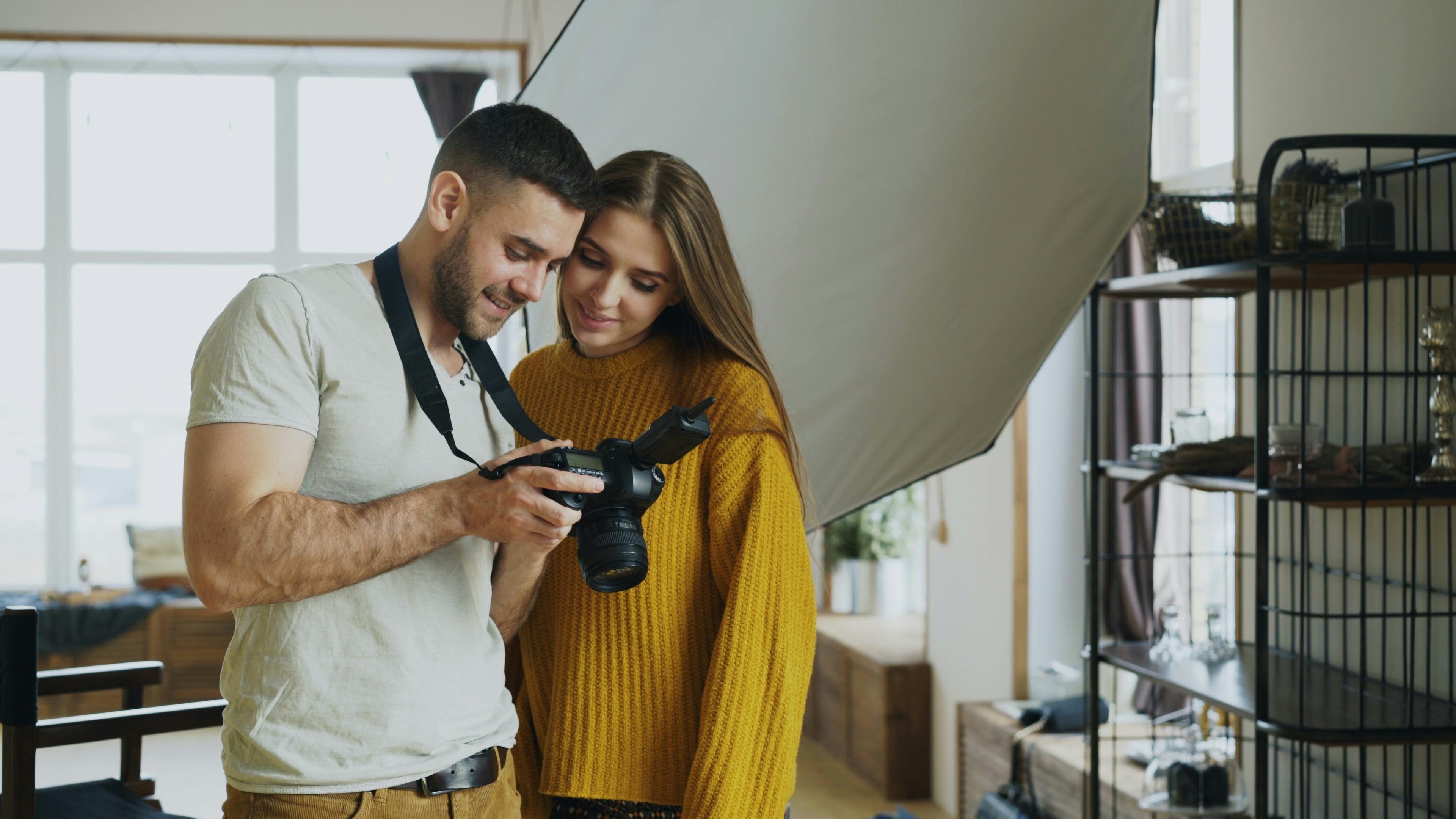 Happy couple reviewing photos on a DSLR camera in a cozy indoor studio.