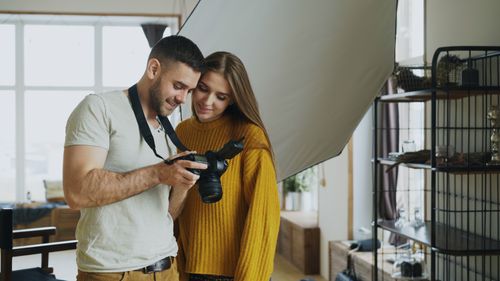 Free Happy couple reviewing photos on a DSLR camera in a cozy indoor studio. Stock Photo