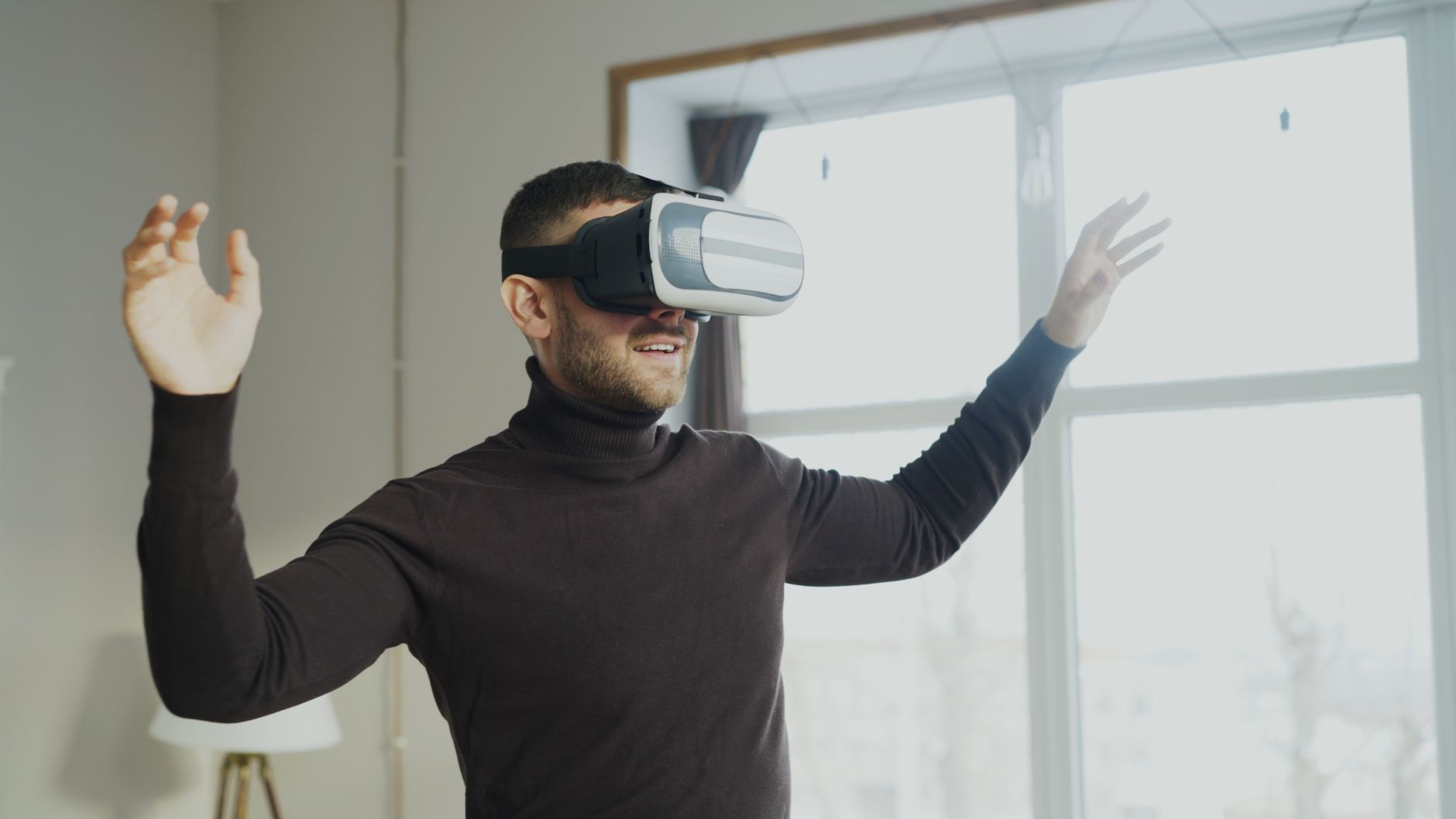 A man using VR goggles, gesturing with excitement indoors.