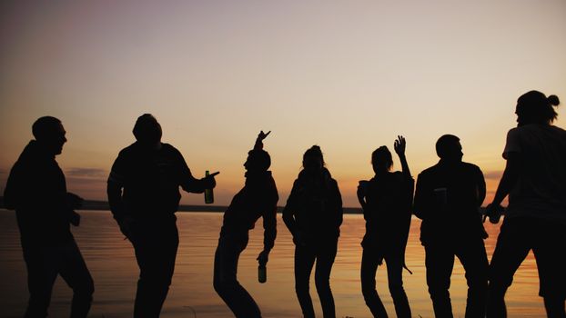 Group of friends silhouetted against a sunset by a lake, enjoying the evening.