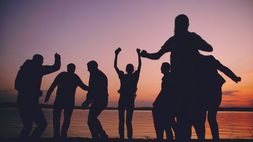Free Group of joyful people dancing by a lake during sunset, creating a lively silhouette. Stock Photo
