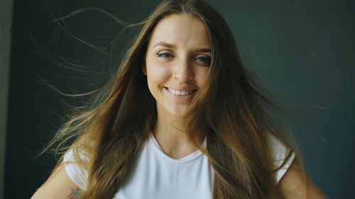 Free Portrait of a young woman smiling with long flowing hair indoors against a dark background. Stock Photo