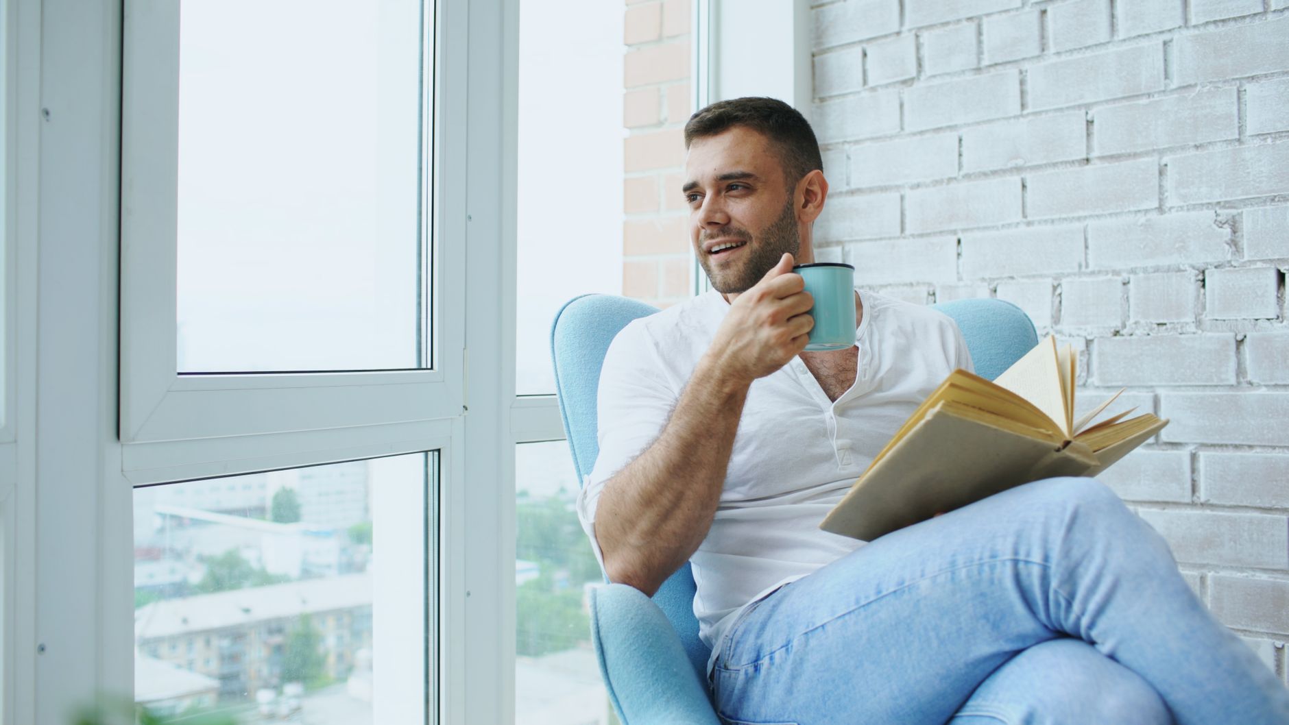 A person relaxing with a book and coffee by a bright window