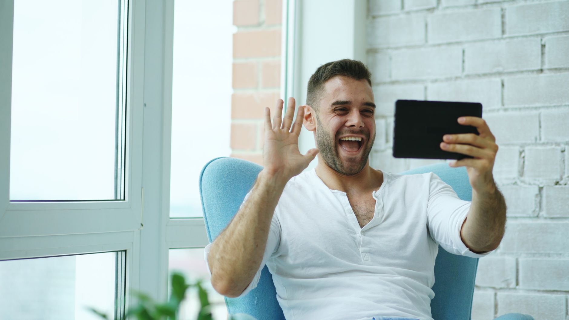 Cheerful man waving during a video call using his tablet indoors.