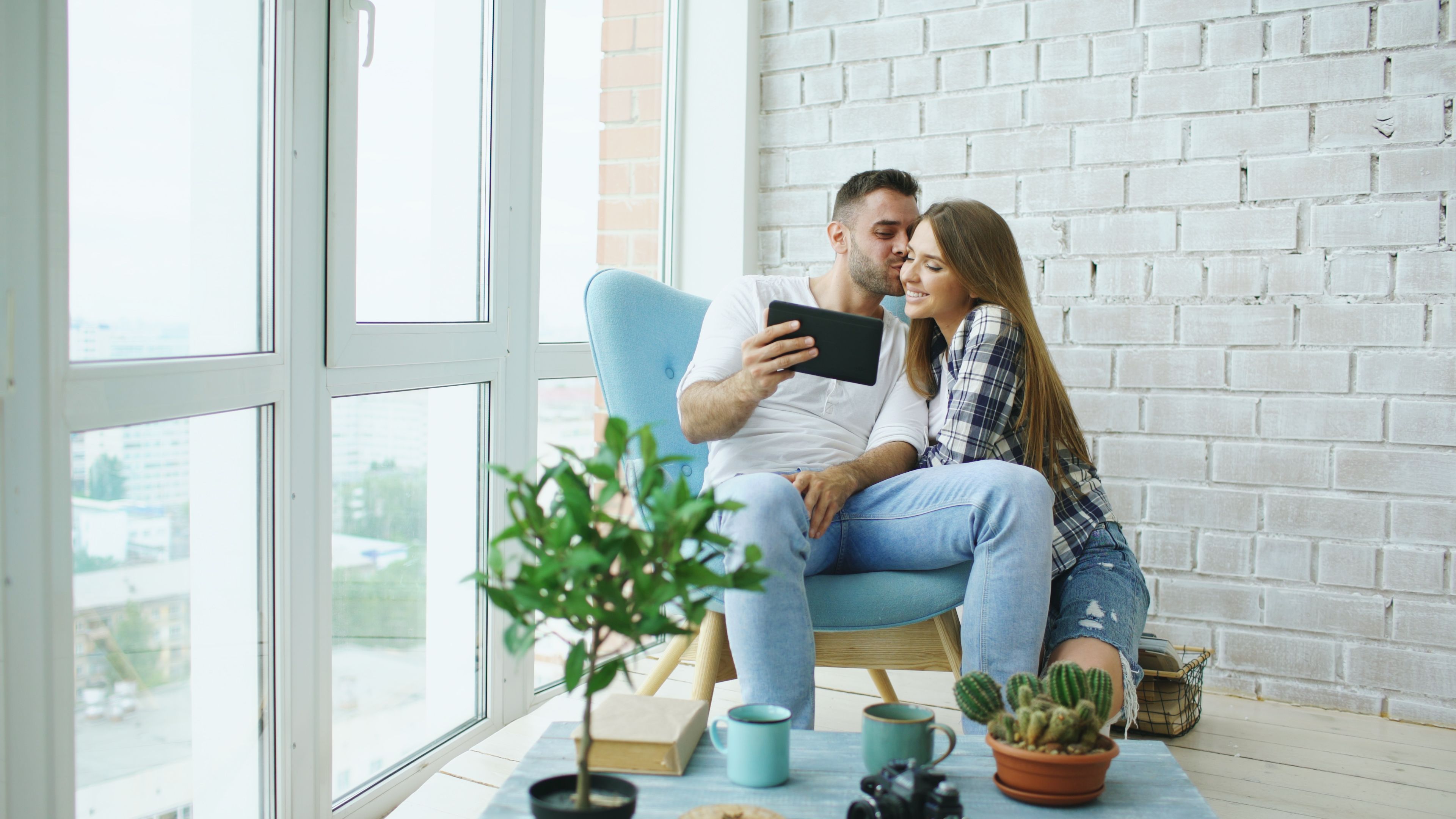 Happy couple sitting in a bright interior, enjoying leisure time with a tablet.