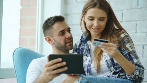 Free Young couple sitting indoors, shopping online with a tablet and credit card. Stock Photo