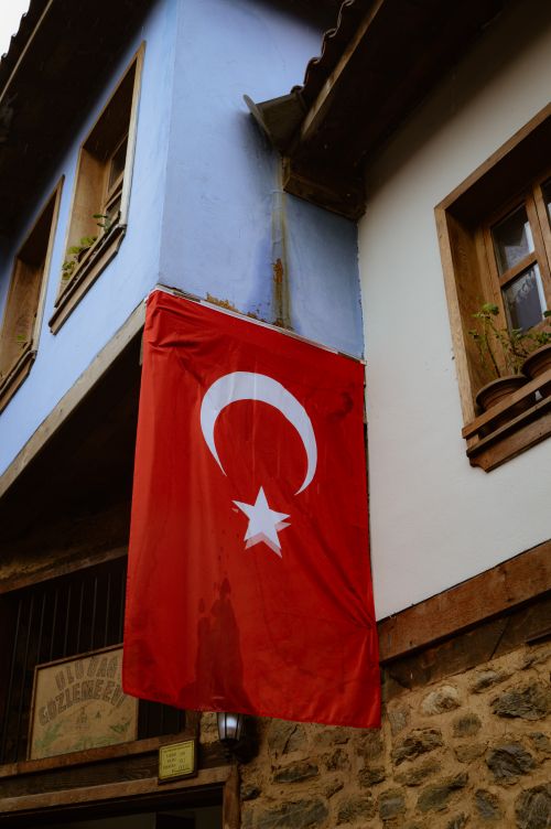 Free A Turkish flag hangs on a historic building with wooden windows and stone walls in a charming neighborhood. Stock Photo