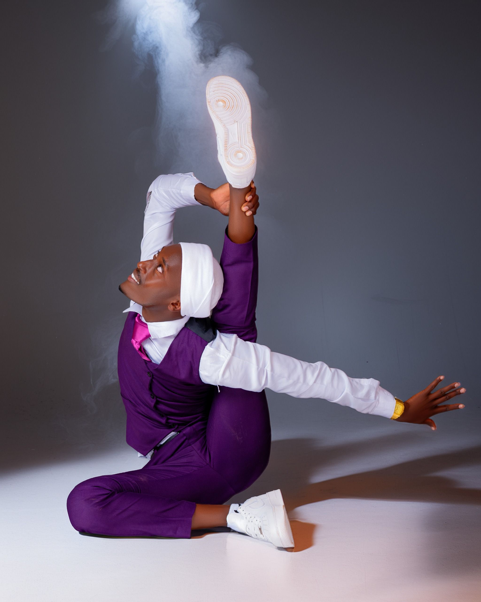 A dancer in a purple outfit shows an impressive flexibility pose indoors.
