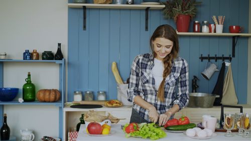 Free Smiling woman chopping vegetables in a cozy kitchen setting. Stock Photo