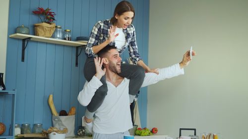 Free Happy couple capturing a fun moment while taking a selfie in a stylish home kitchen. Stock Photo