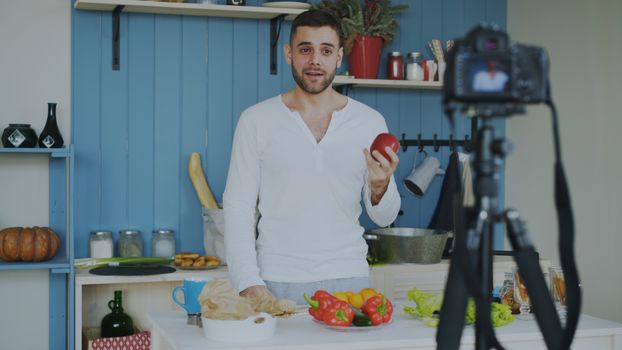 Young man filming a cooking video in a stylish kitchen with fresh ingredients.