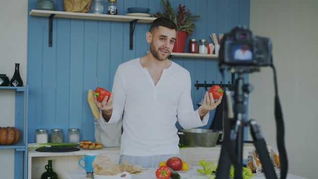 Man in kitchen filming cooking video with fresh vegetables. Lifestyle content creation.