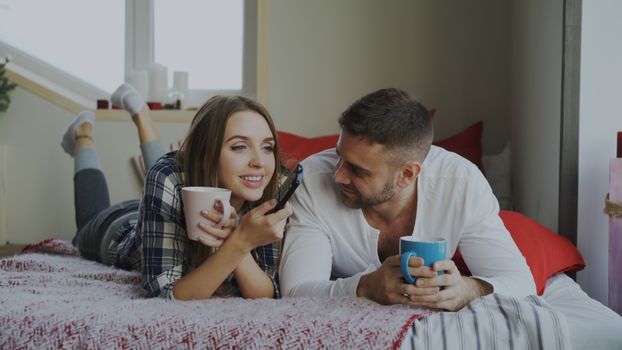 Happy couple enjoying coffee and chatting indoors in a cozy bedroom.