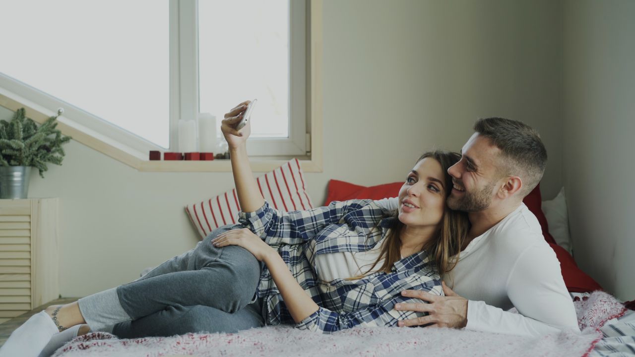 Couple relaxing on a bed, the woman in a plaid pajama shirt