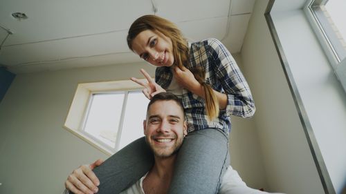 Free Young couple joyful indoors, piggyback and smiling in airy room. Stock Photo