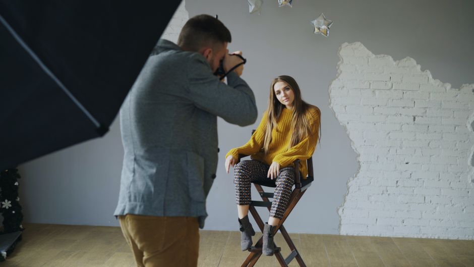 Stylish woman sits for a photoshoot in a modern studio with a photographer.