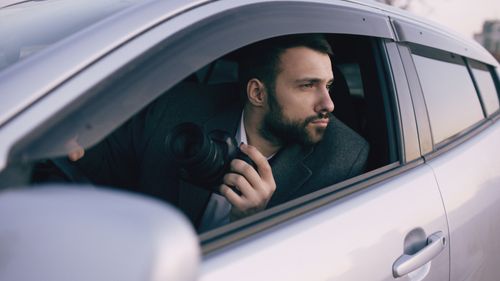 Free Man with a camera looking out of car window capturing a scene. Ideal for photography and exploration themes. Stock Photo