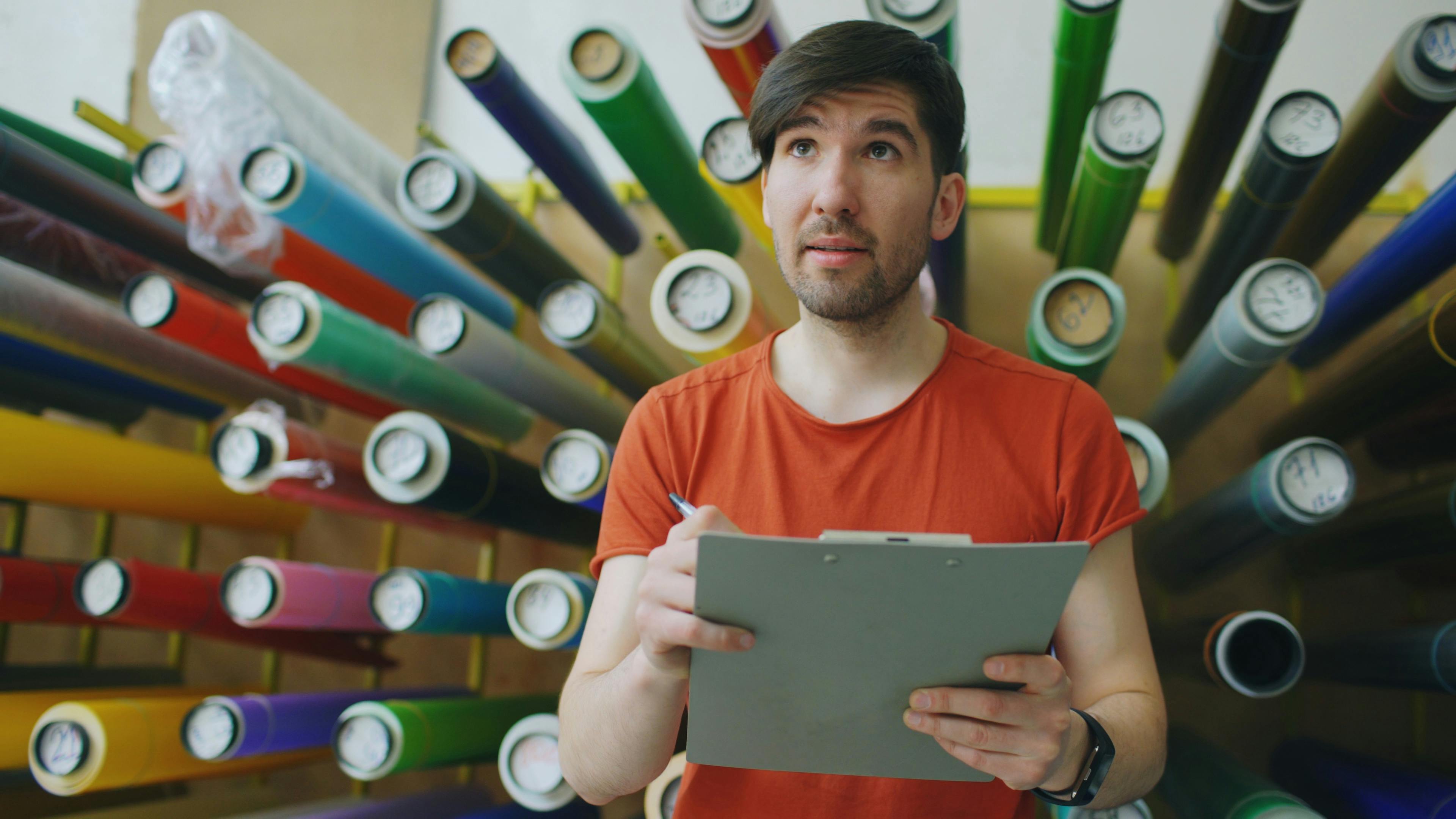 Young man in a vibrant workshop examining materials with a clipboard.