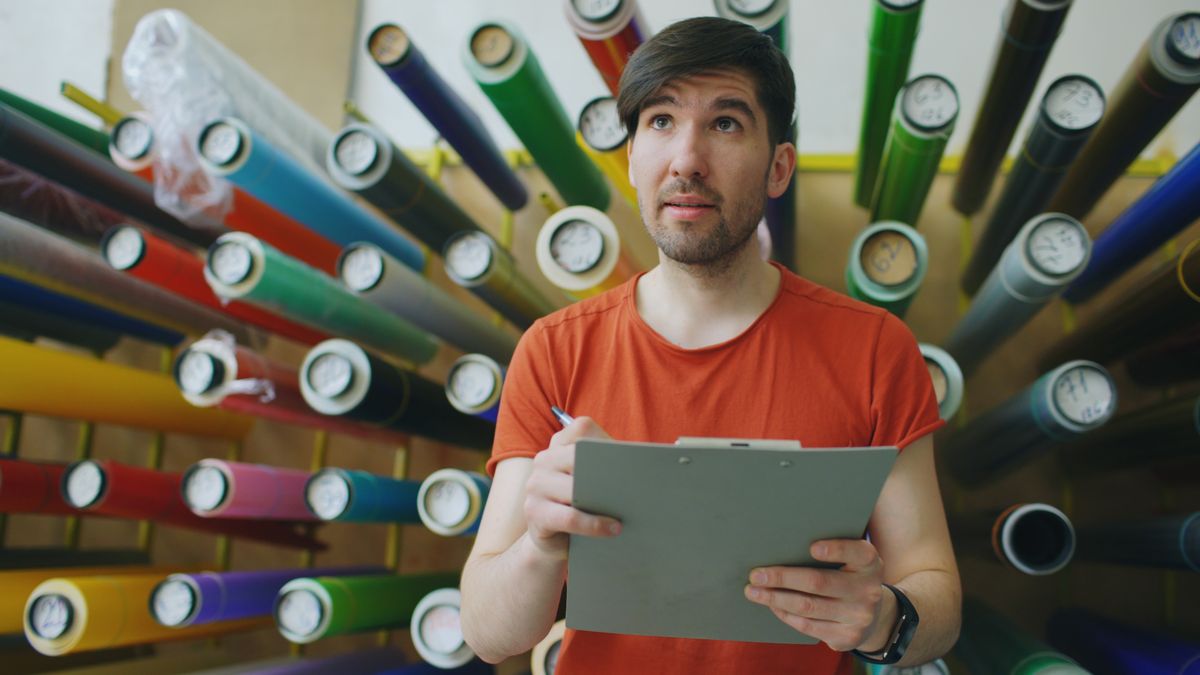 A man with a clipboard checking stock among racks of colored vinyl rolls