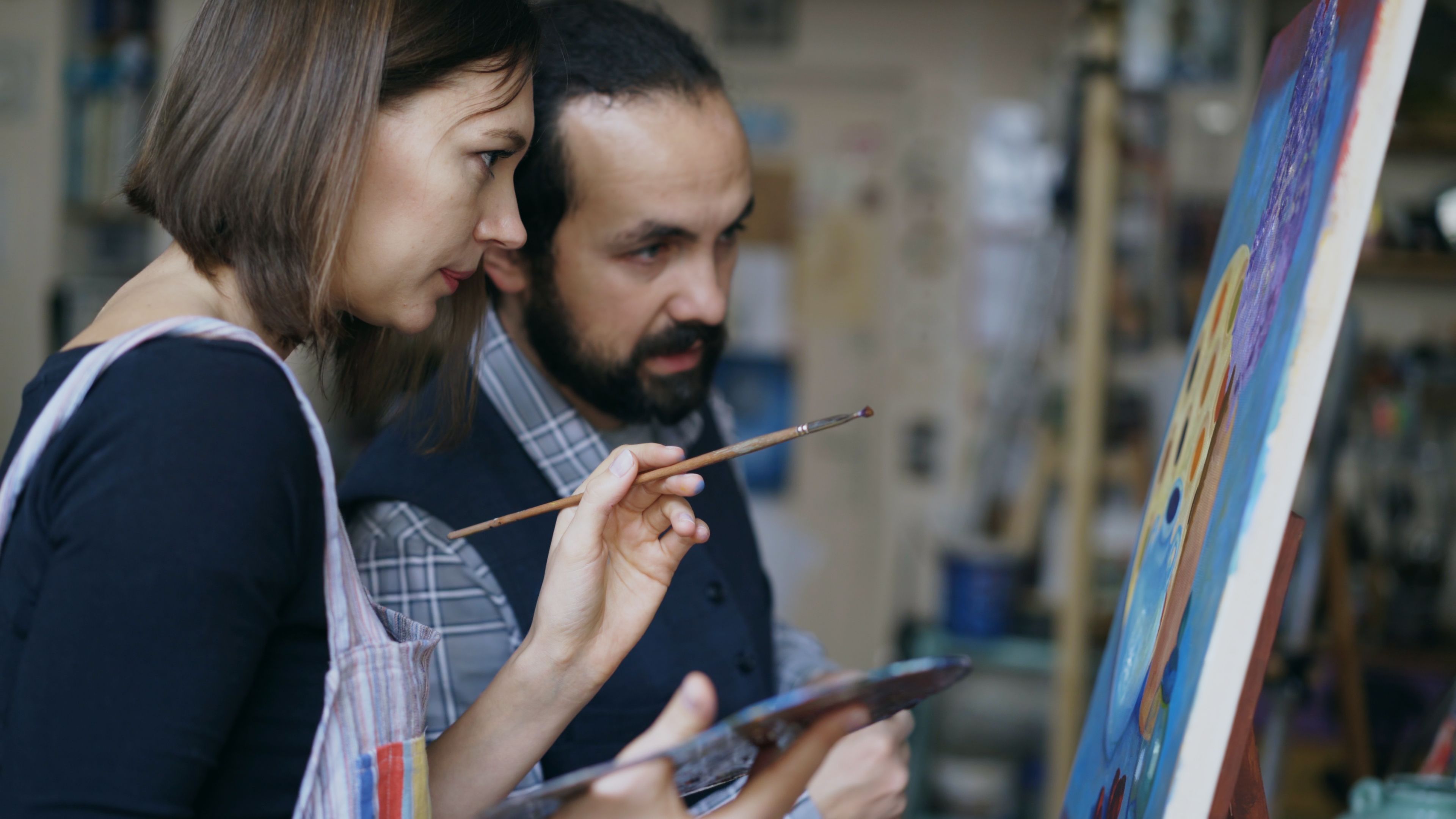 2人のアーティストが美術スタジオで色鮮やかな絵画を共同制作し、創造的なチームワークを発揮している。