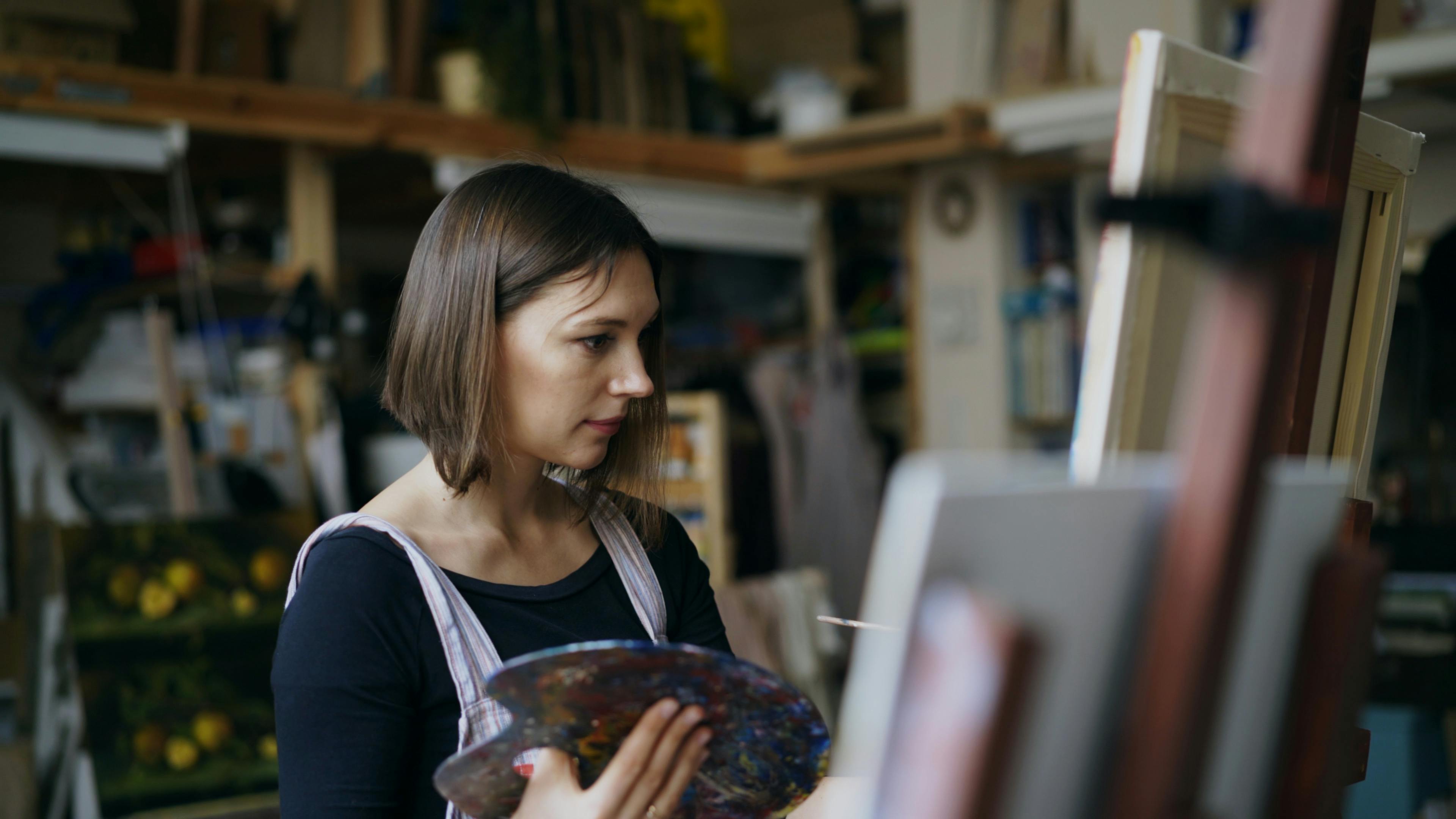 Woman artist painting on canvas in a studio with artistic tools.