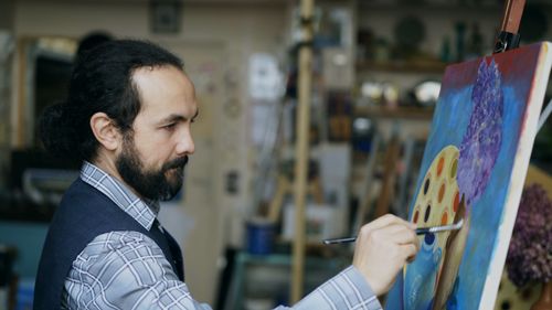Free Artist carefully painting a vibrant canvas in a well-lit studio. Stock Photo