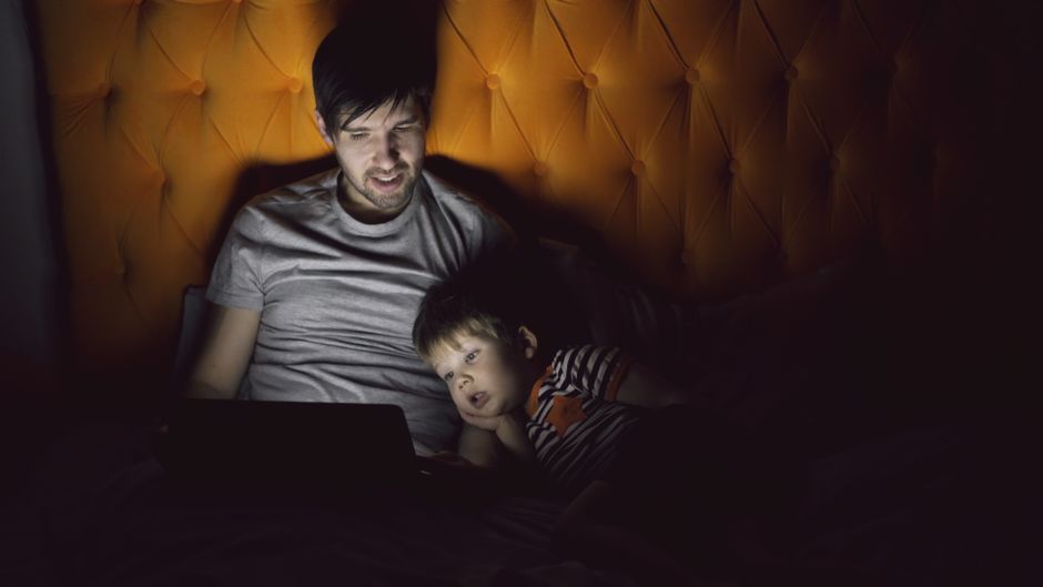 A father and his child sharing a quiet moment at night illuminated by a tablet.