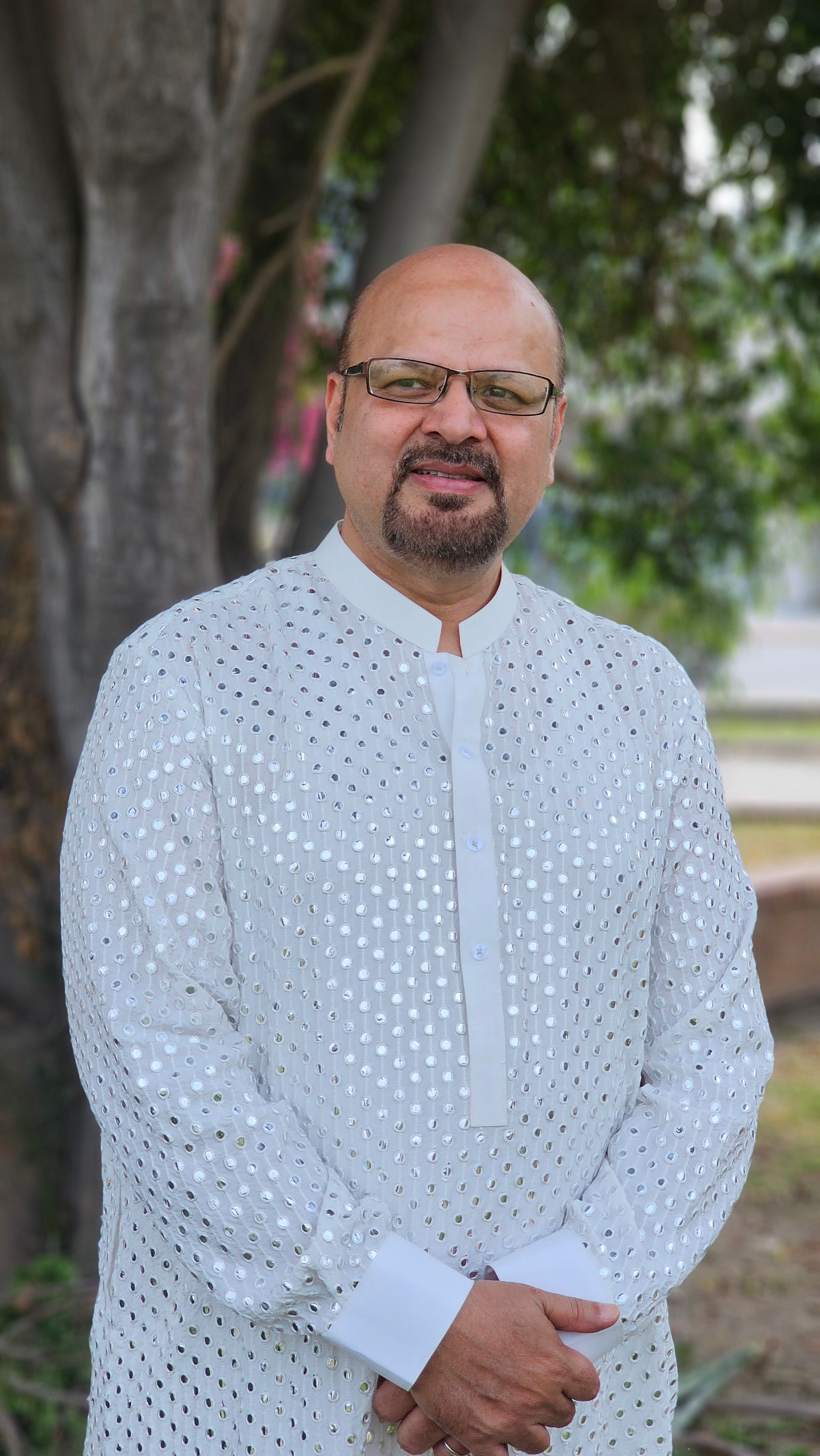 Portrait of a man wearing traditional clothing standing near a tree outdoors.