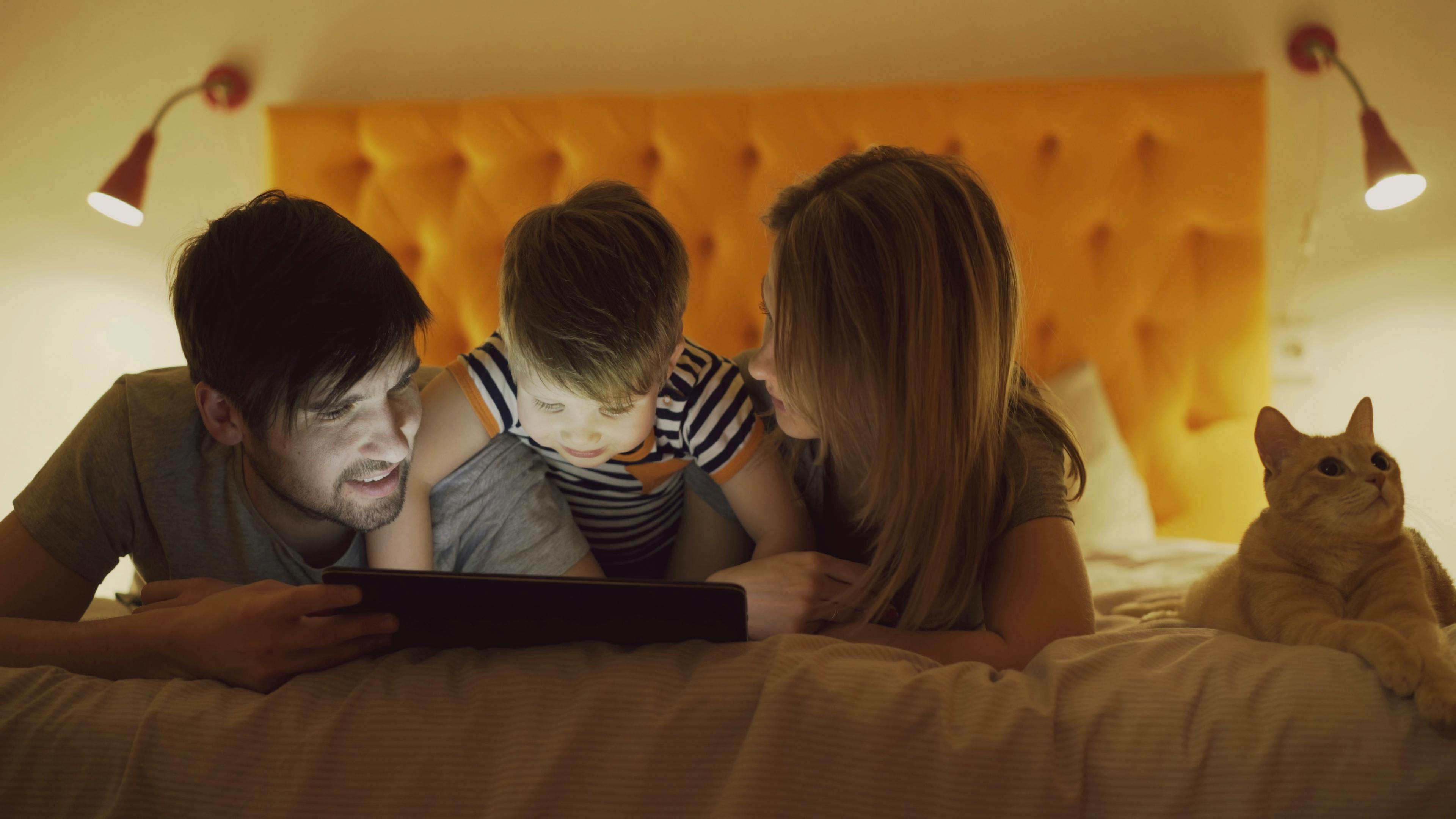 A family enjoying quality time in bed with their pet cat.