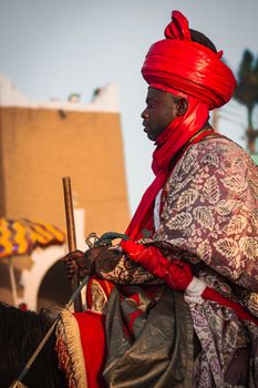 African man in vibrant ceremonial attire on horseback, showcasing cultural heritage.