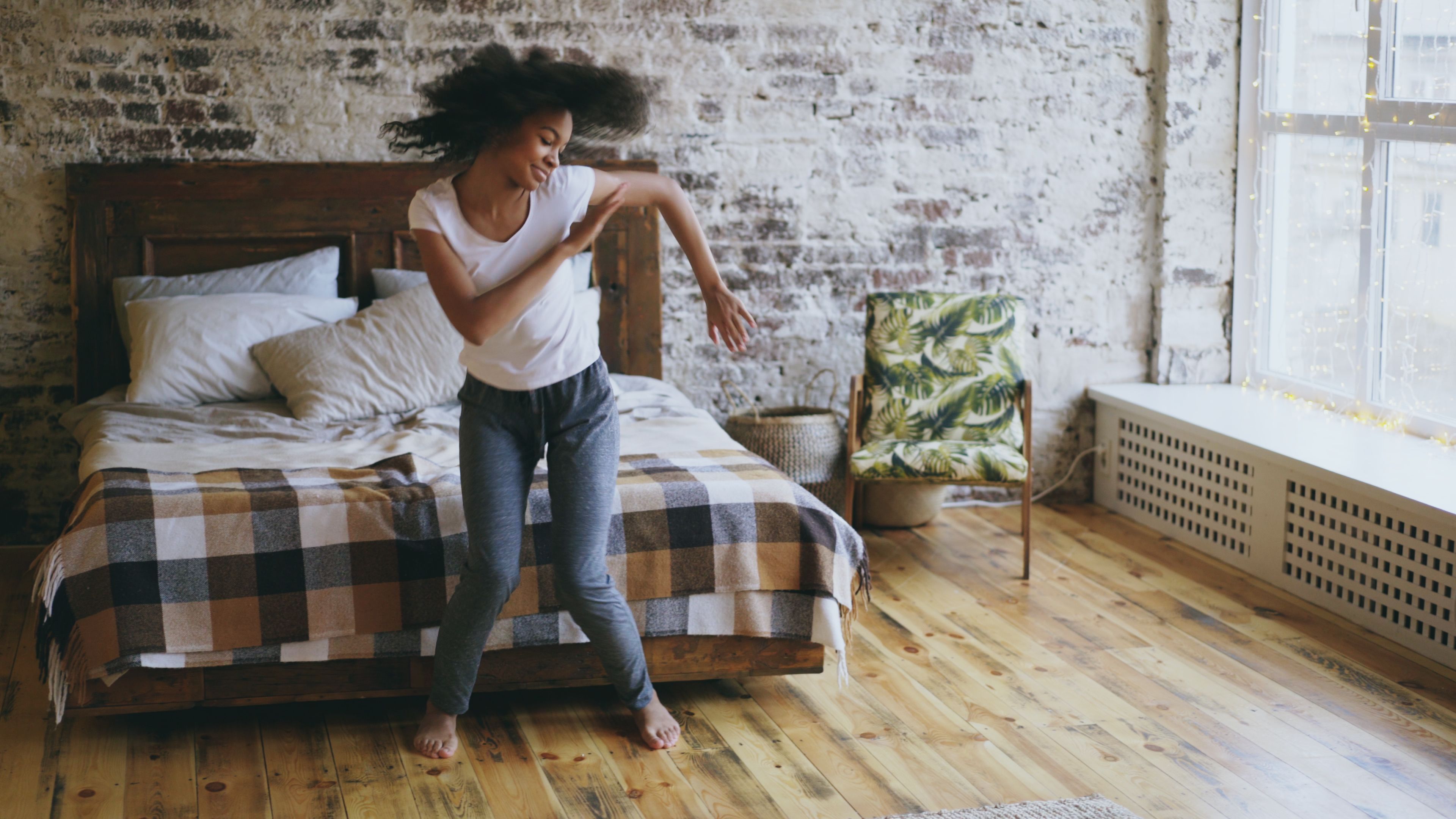Young woman dancing joyfully in a rustic bedroom with natural light.