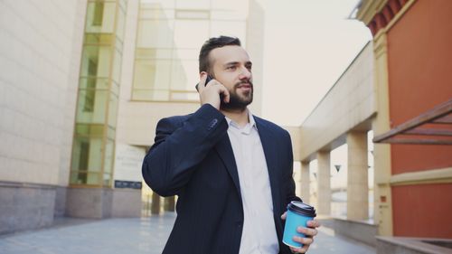 Free Confident businessman with coffee cup talking on phone outdoors. Stock Photo