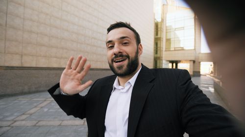 Free Smiling businessman waving in urban environment, business communication concept. Stock Photo