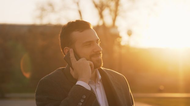 Smiling man using smartphone outside during sunset, with golden light creating a warm atmosphere.