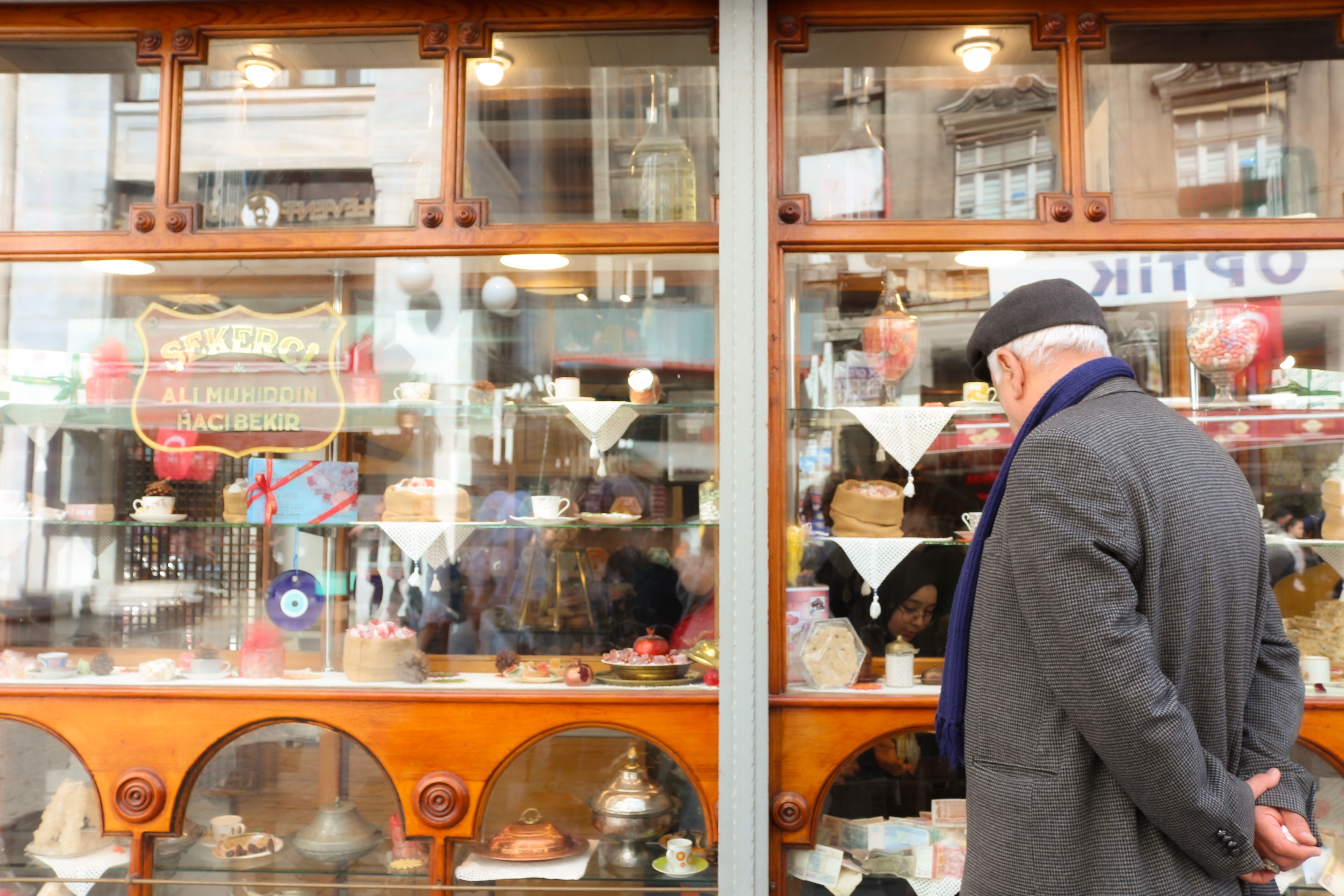 Senior man gazes at a vintage Istanbul bakery window displaying Turkish delights.