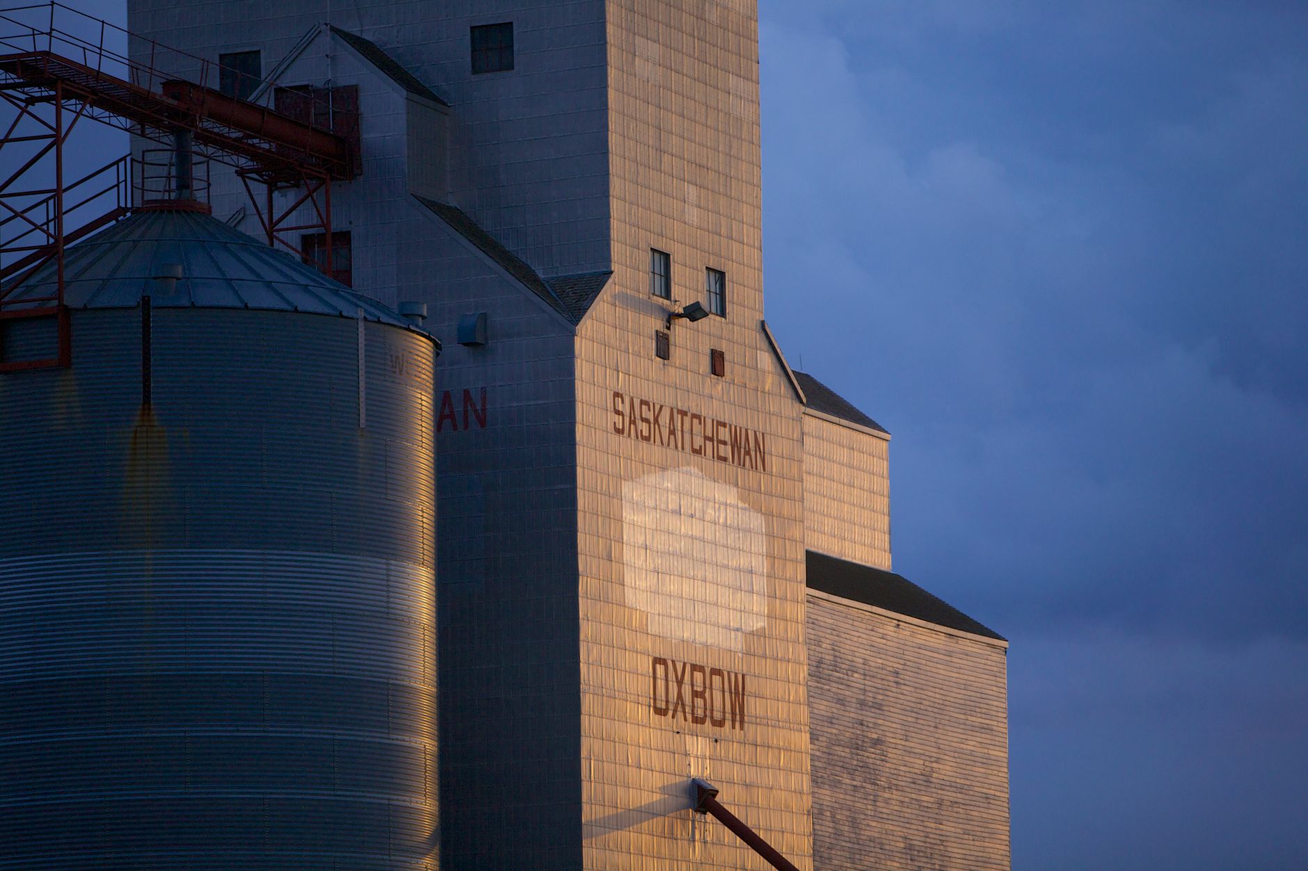 Grain silos in Oxbow, Saskatchewan, Canada, captured under evening light with dramatic sky.
