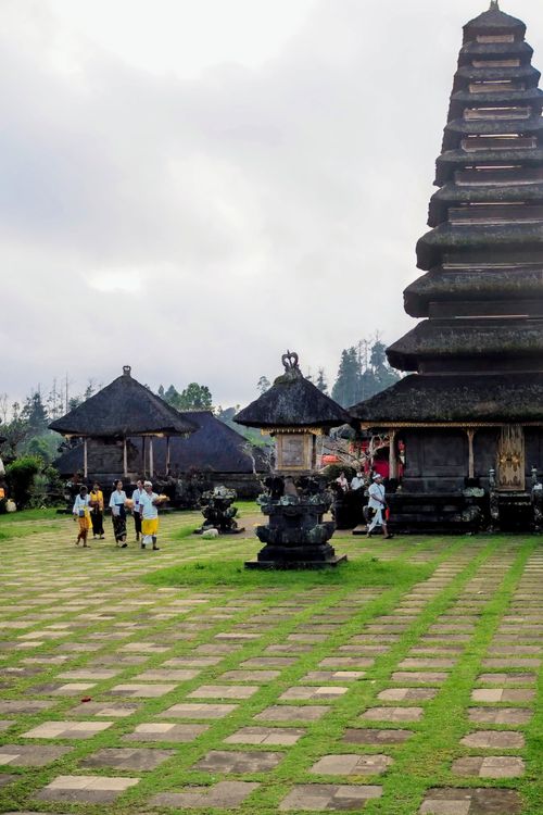 Free Balinese temple with pagoda and people in traditional attire on a cloudy morning. Stock Photo