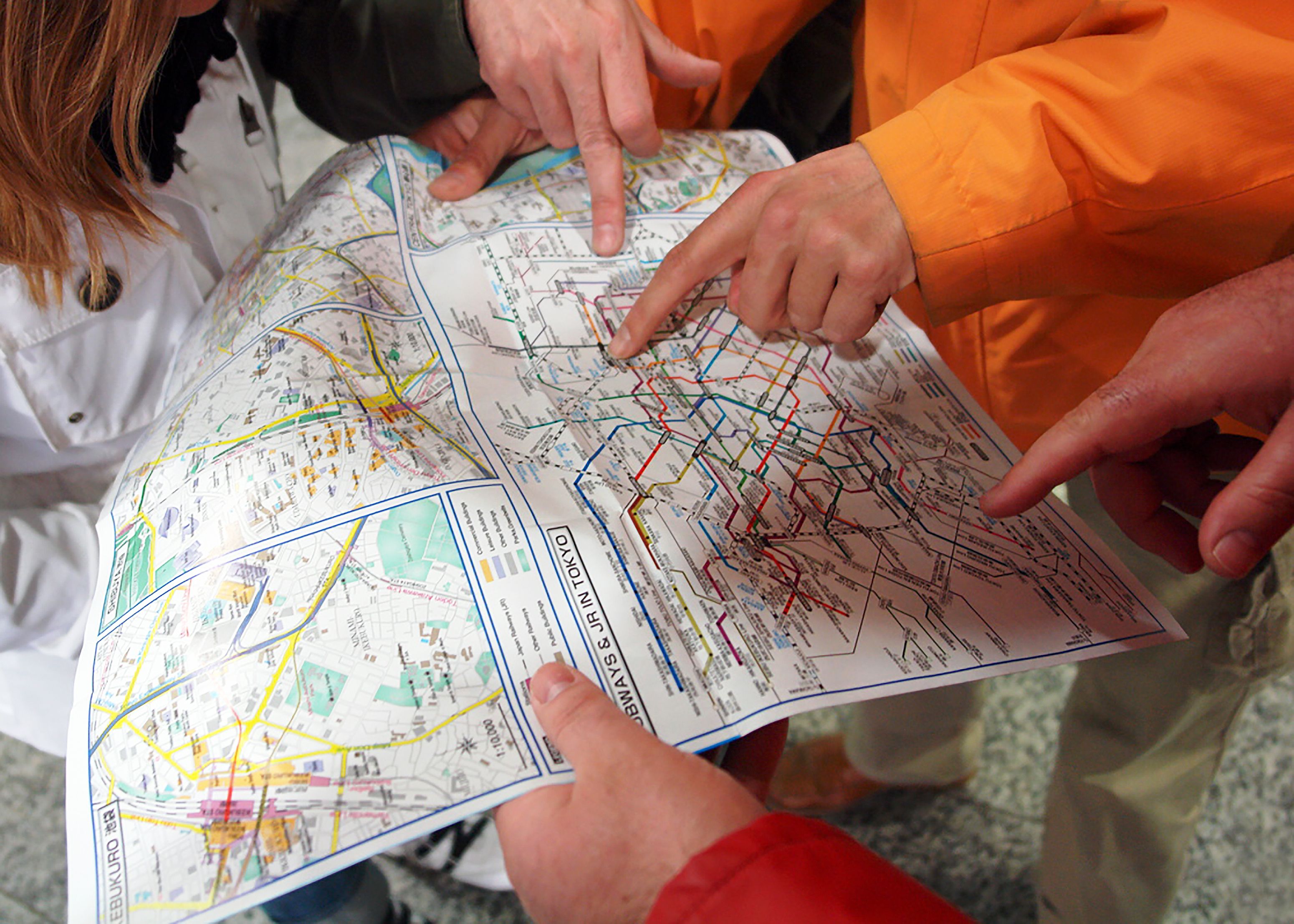 Group of people pointing at a Tokyo subway map, planning their route in Japan's capital city.