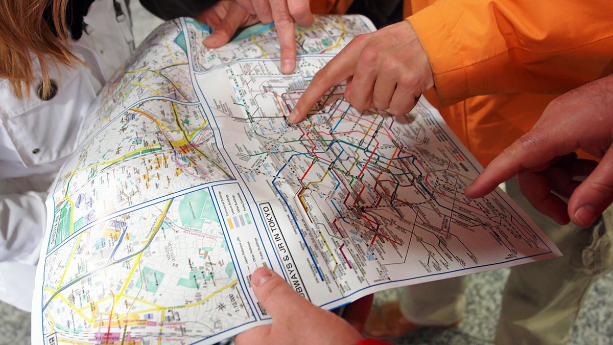 Group of people pointing at a Tokyo subway map, planning their route in Japan's capital city.