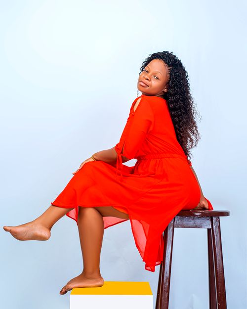 Free Elegant woman in a red dress sitting gracefully on a wooden stool. Stock Photo