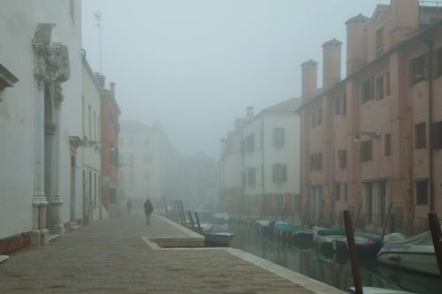 Free A lone figure walks along a foggy canal in Venice, offering a serene and atmospheric scene. Stock Photo