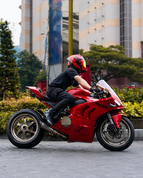 Free A vibrant red Ducati motorcycle ridden by an adult on a city street, showcasing speed and style. Stock Photo