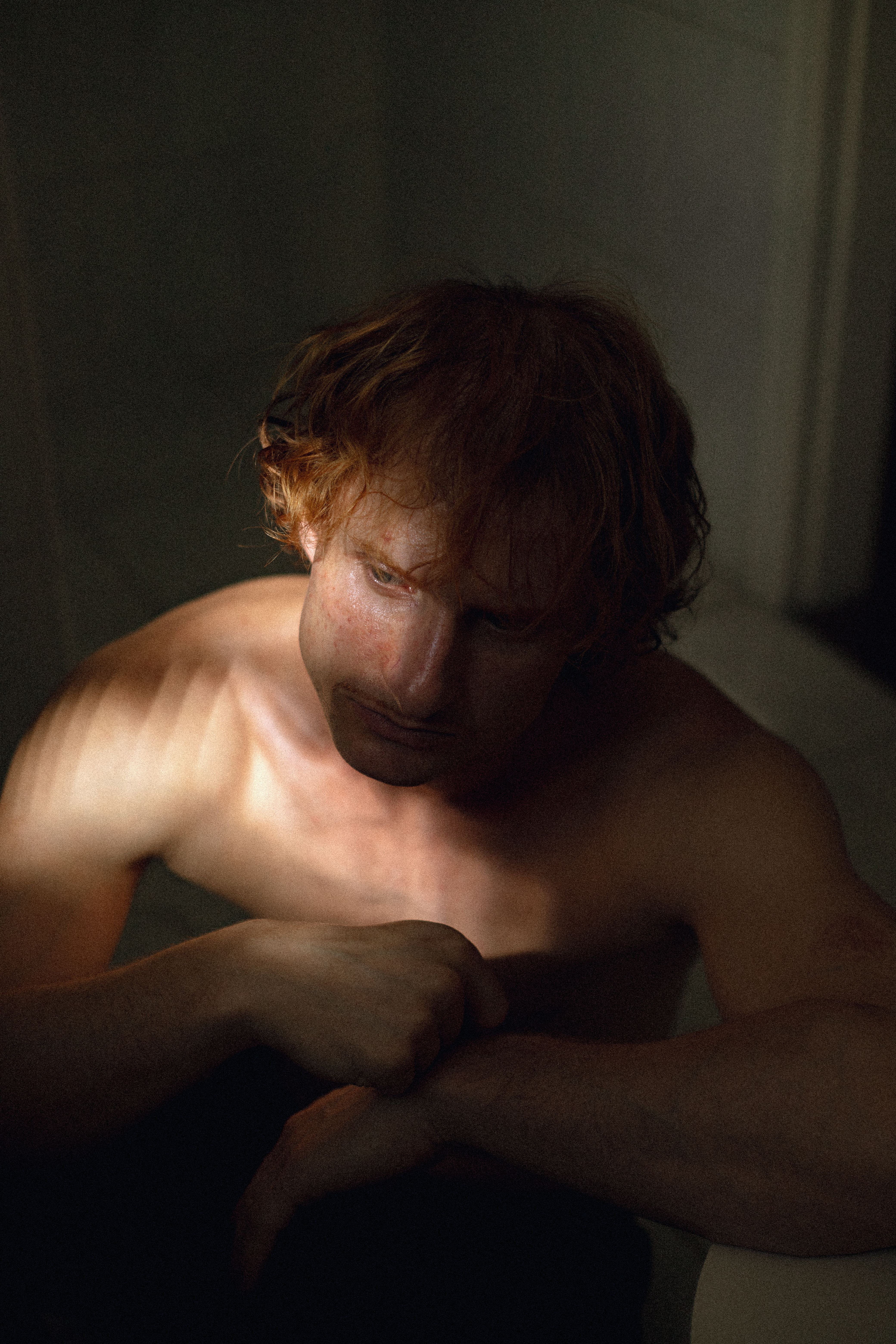 A contemplative man in dim indoor lighting casts a reflective and moody expression.