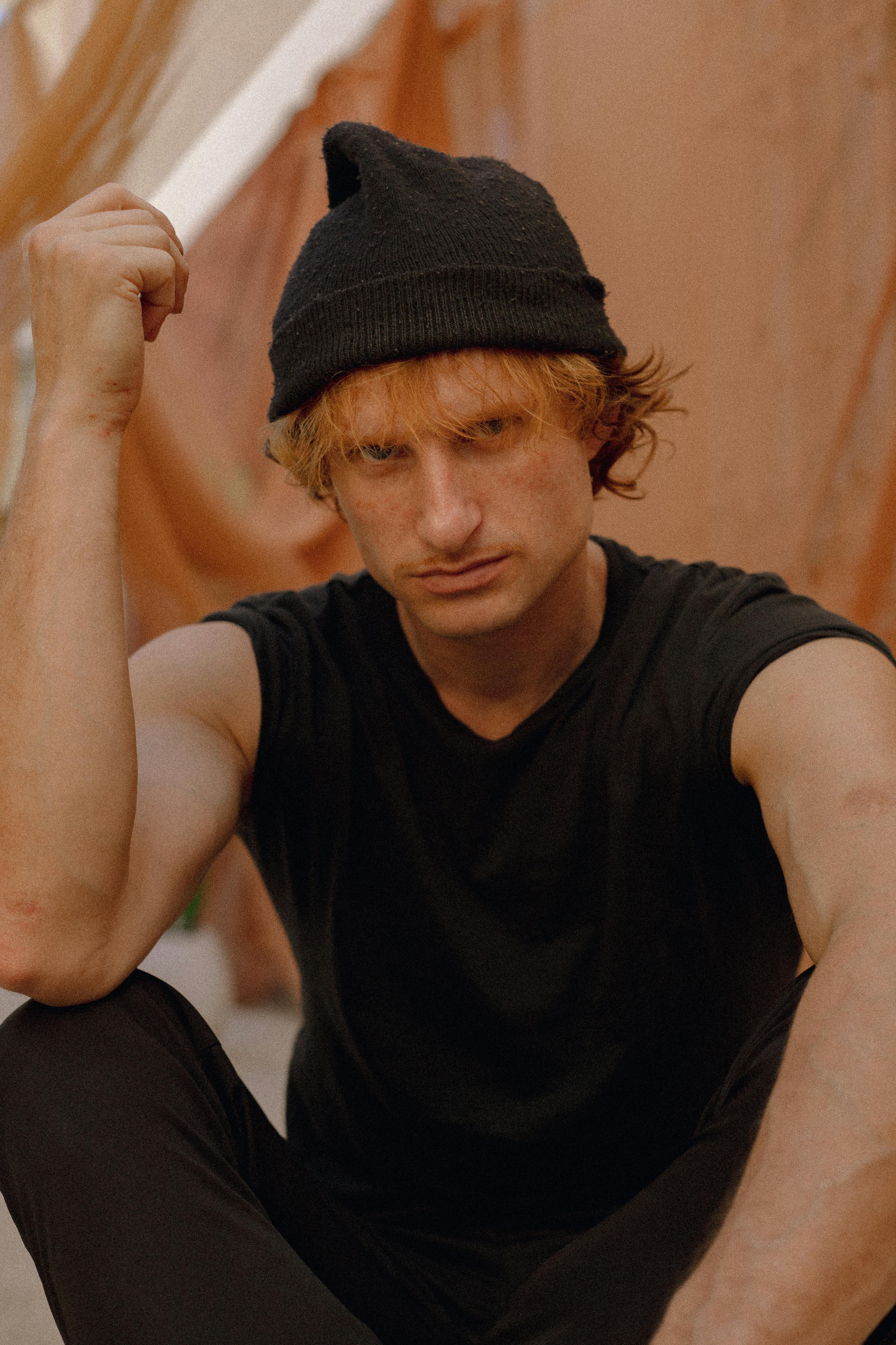 A young man with a beanie sits outdoors, exuding a moody fashion vibe. Perfect for lifestyle and fashion concepts.
